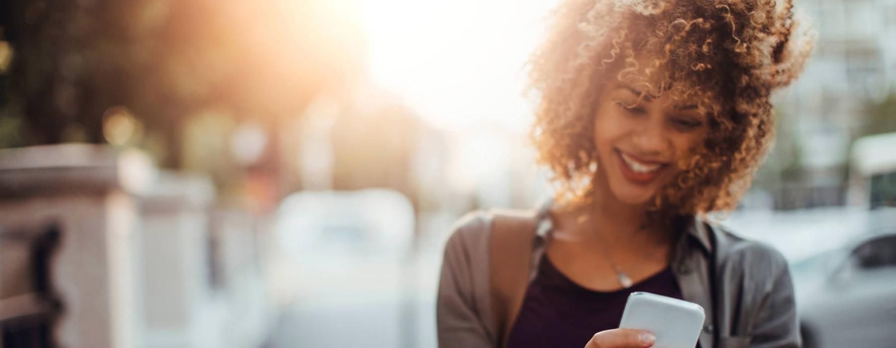 woman texts on her phone as she walks through the city